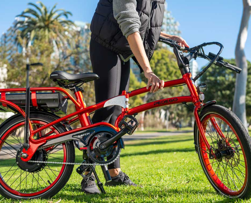 The new V2 Pedego Latch Folding Bike in red with a happy cyclist in an urban setting.