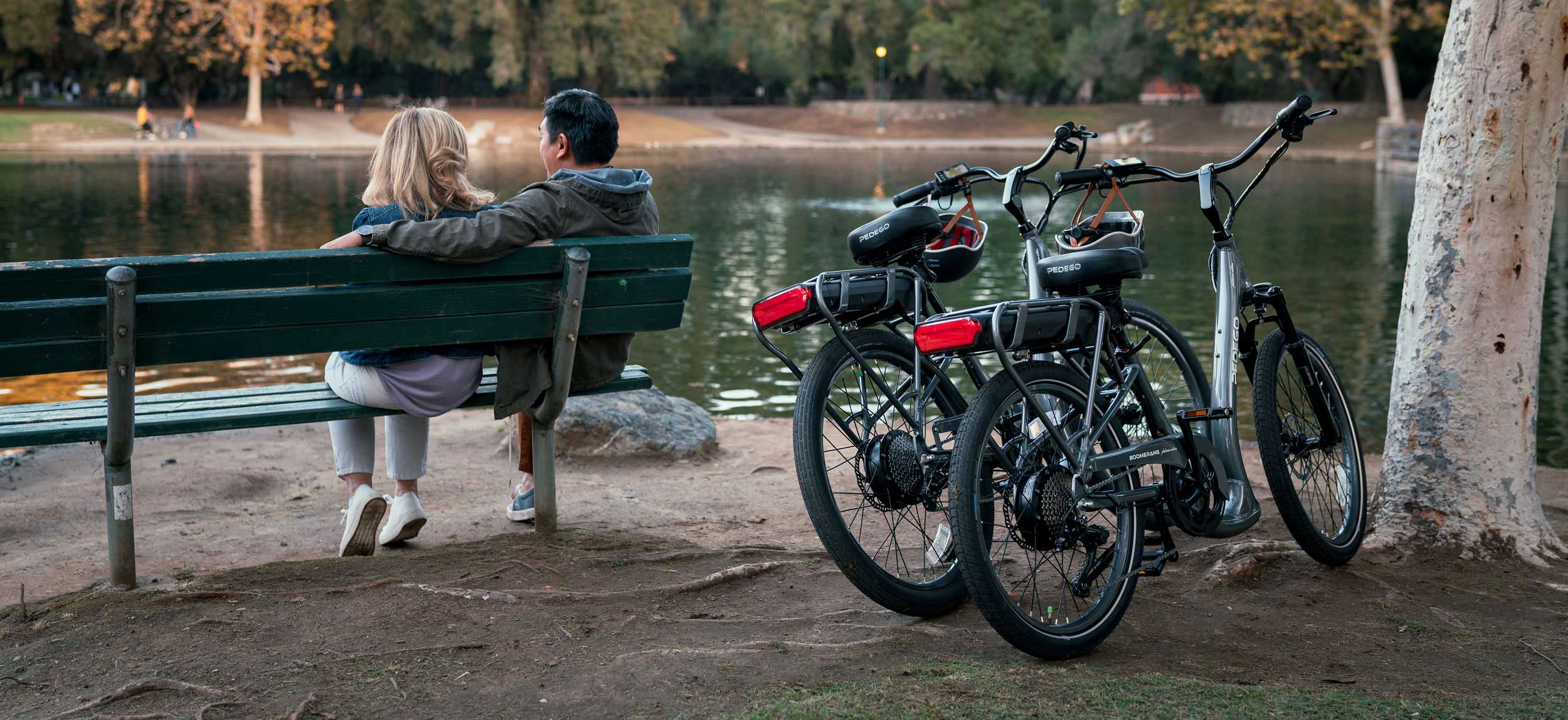 New-Pedego-Battery-on-Platinum-Boomerang-Electric-Bike-2 Couple sitting lakeside with pedego electric bikes parked
