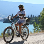 Happy woman riding white pedego electric bike on a lakeside trail.